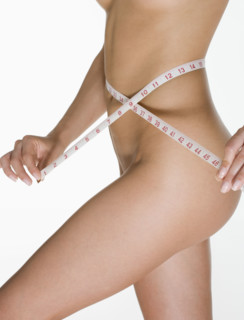 Nude female measuring her waist.