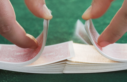 Hands shuffling cards on poker table.