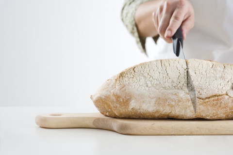 Hand cutting loaf of bread.