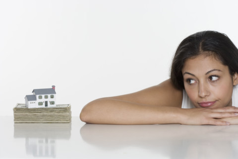 Woman looking at miniature house and money.