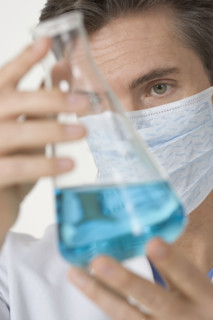 Masked scientist examining blue liquid.