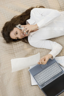 Businesswoman on mobile phone while lying on bed.