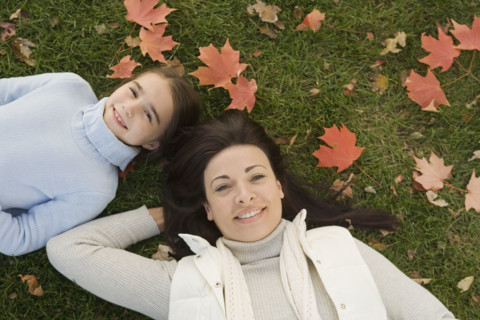 Mother and daughter lying on grass on fall day.