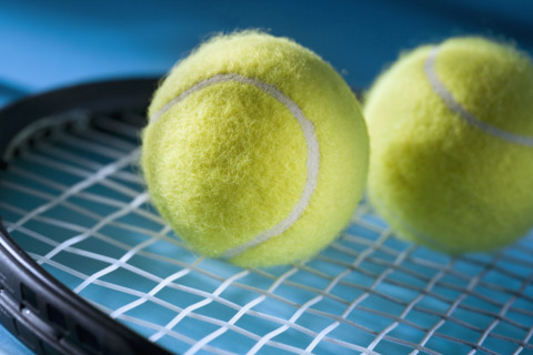 Closeup of tennis racquet and two balls.