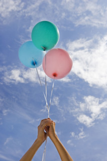 Hands holding balloons toward sky.
