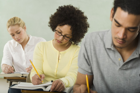Three college students in class taking test.