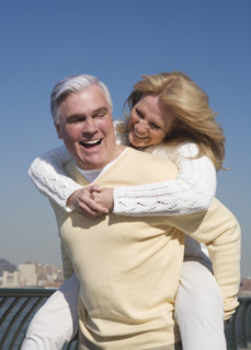 Senior man giving senior woman piggy back ride outdoors.