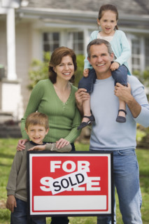 Family in front of house with For Sale/Sold sign.