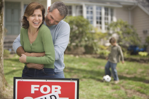 Family in front of house with For Sale/Sold sign.