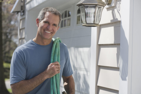 Man holding hose in front of garage.