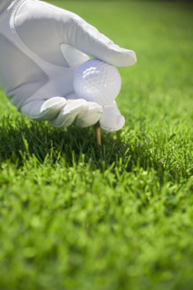 Gloved hand placing golf ball and tee into turf.