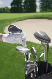 Hand selecting golf club with course in distance.
