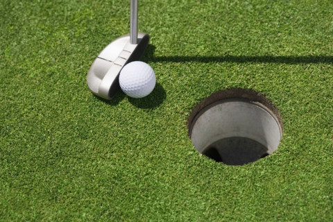 Golf ball near cup on putting green outdoors.