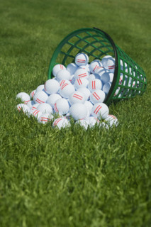 Basket of golf balls spilling onto grass.