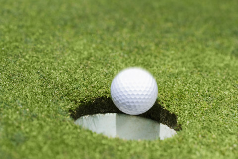 Golf ball dropping into hole on green.