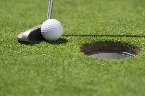 Closeup of golf ball and club near cup.