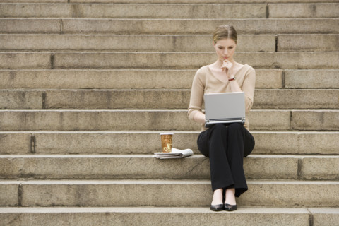 Young woman sitting outdoors on stairs with laptop.
