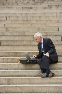 Man sitting outdoors on stairs with laptop.