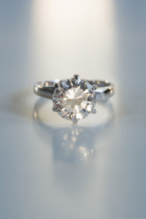 Diamond like ring in six pronged silver setting on table.