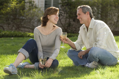 Couple sitting in grass drinking wine.