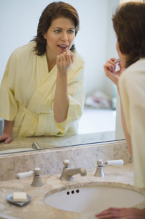Woman putting on lipstick in bathroom.