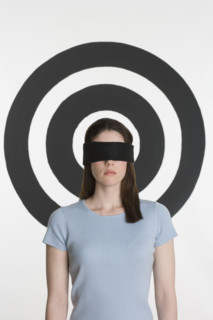 Blindfolded woman standing in front of bull’s eye.