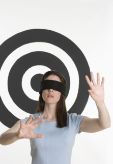 Blindfolded woman standing in front of bull’s eye.