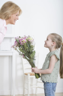 Young granddaughter giving grandmother bouquet of flowers.