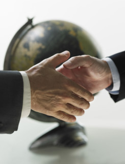 Two men shaking hands with globe in background.