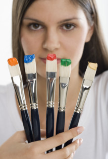 Paintbrushes with paint in front of woman's face.