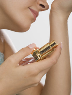 Close up of woman holding perfume and smelling wrist.