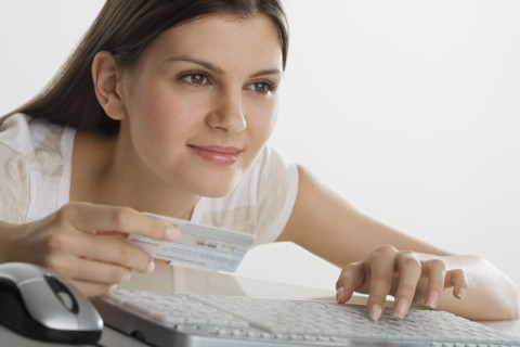 Woman holding credit card and using computer keyboard.