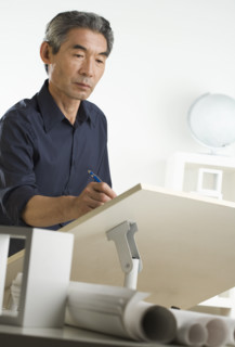 Asian businessman at drafting table with blueprints.