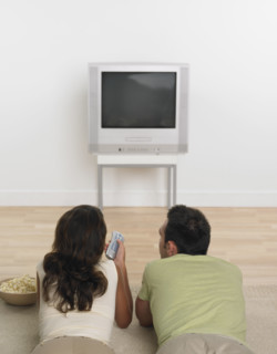 Couple laying on floor with popcorn watching television .