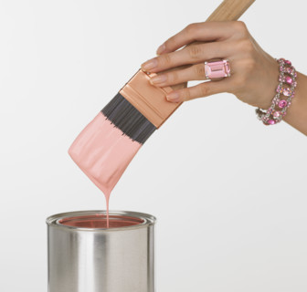 Woman's jeweled hand dipping paintbrush in paint can.