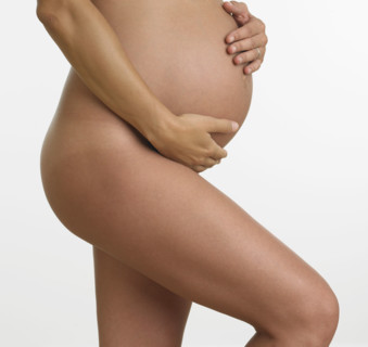 Studio shot of nude pregnant woman holding stomach.