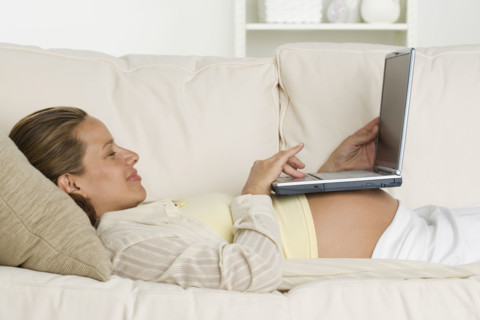 Pregnant woman on sofa using laptop.