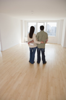 Rear view of couple with blueprints in empty room.