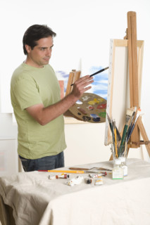 Man painting at easel indoors.