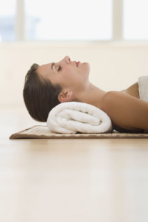 Woman laying on mat with rolled towel under neck.