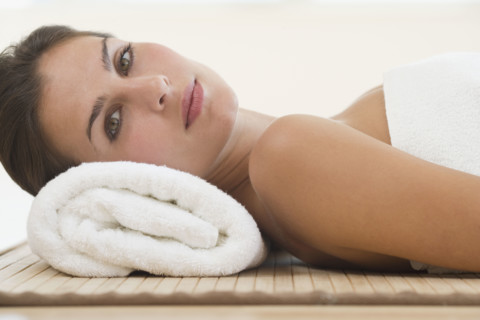 Woman laying on mat with rolled towel under neck.
