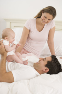 Parents playing with baby in bed.