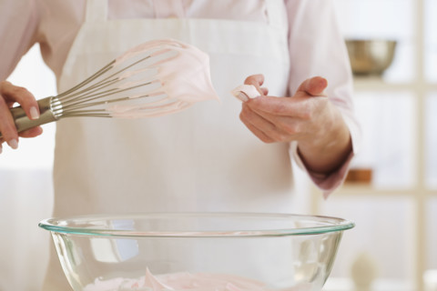 Woman wiping batter from whisk with finger.