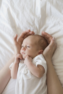 Mother holding hands around newborn baby's head.