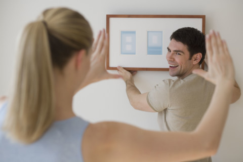 Couple hanging picture on wall.