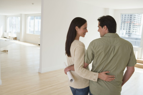 Couple hugging and holding blueprints in empty house.