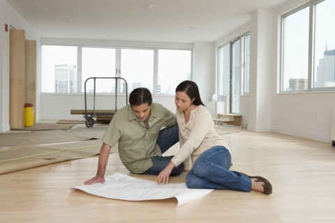 Couple looking at blueprints on floor in new house.