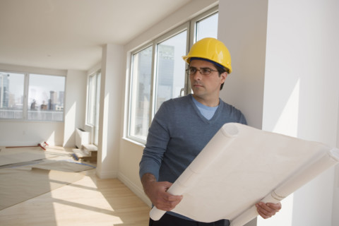 Man wearing hard hat and holding blueprints in house.