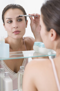 Woman combing eyebrows in mirror.
