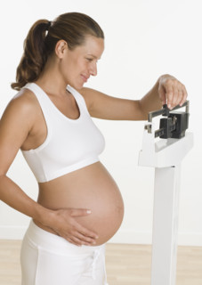 Pregnant woman weighing self on scale.